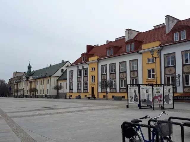 The image shows a city square with bicycles parked in front of a building with windows, light...