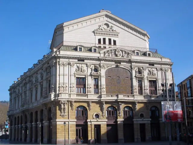 The image shows a large building with a lot of windows on the side of it, surrounded by street...