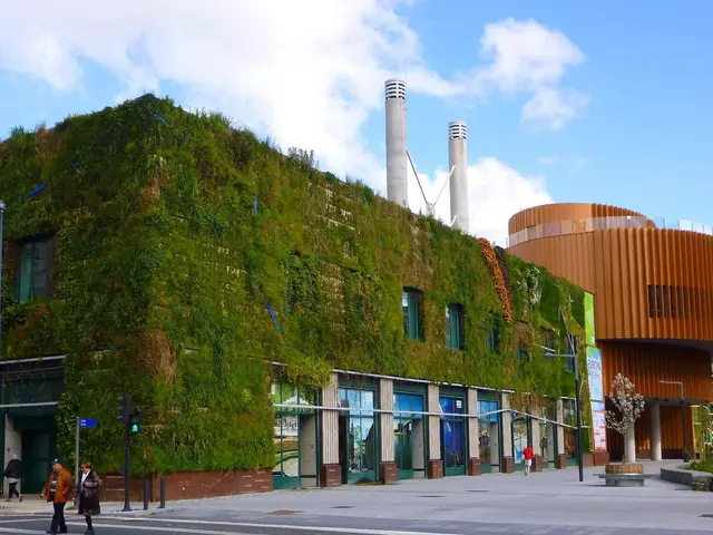 The image shows a large building with a green wall on the side of it, surrounded by street poles,...