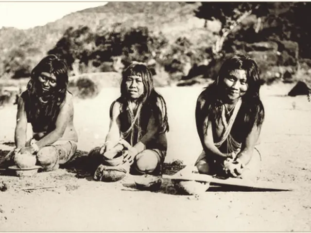 The image shows three Native American women sitting on the ground in the desert, surrounded by...