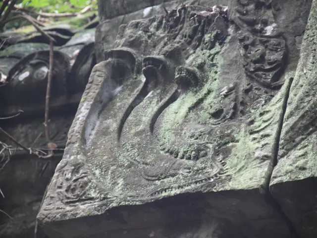 The image shows a stone carving on the side of a building in Angkor Thom, Cambodia. The carving is...