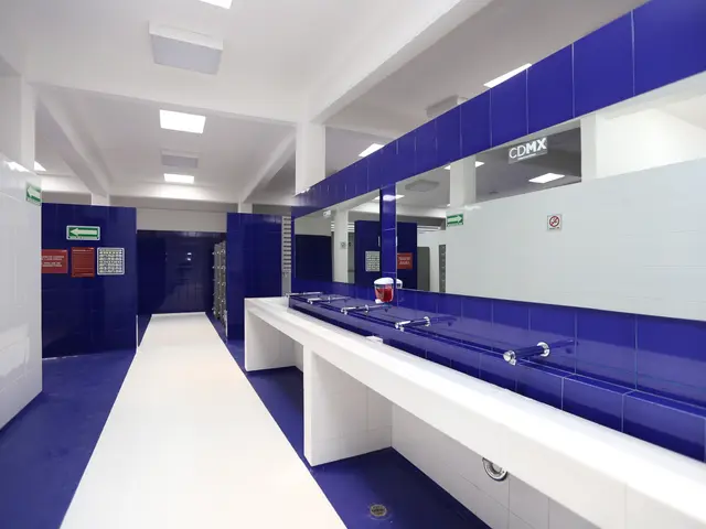 The image shows a public restroom with blue tiled walls and white counter tops. There are sinks...
