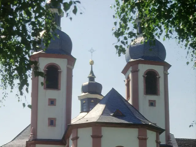 The image shows a church with two towers in the middle of a park, surrounded by buildings, street...