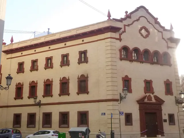 The image shows a large building with a lot of windows on the side of it, surrounded by street...