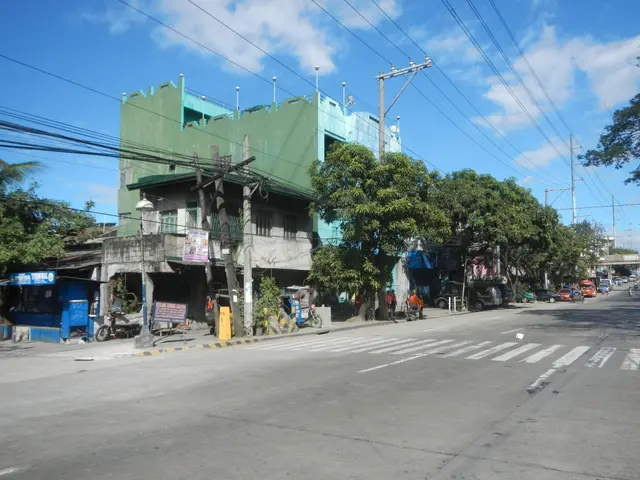 The image shows a city street with a green building on the side of it. There are vehicles driving...