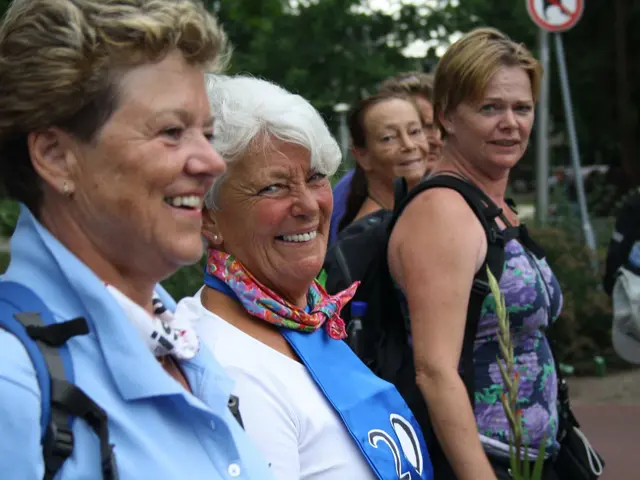 The image shows a group of women standing next to each other on a sidewalk, smiling. In the...