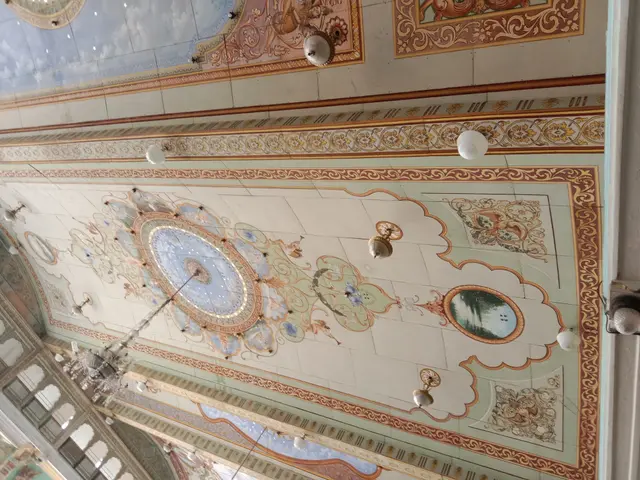 The image shows the interior of a building with a beautiful ceiling adorned with intricate designs...