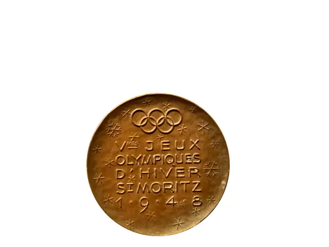 The image shows a gold medal with the Olympic logo on it against a white background. The medal is...
