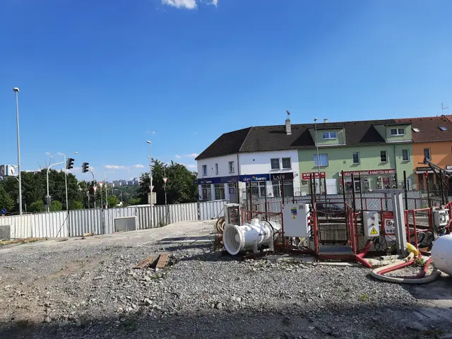 The image shows a construction site with a lot of pipes and equipment on the ground, surrounded by...