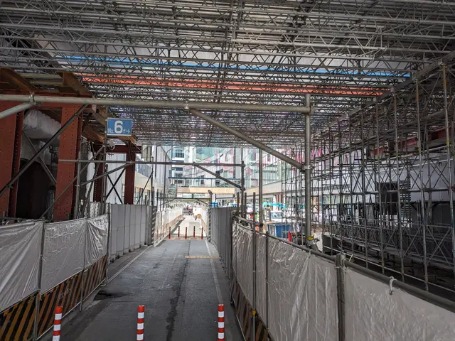 The image shows a construction site with a lot of scaffolding on the side of it, including poles, a...