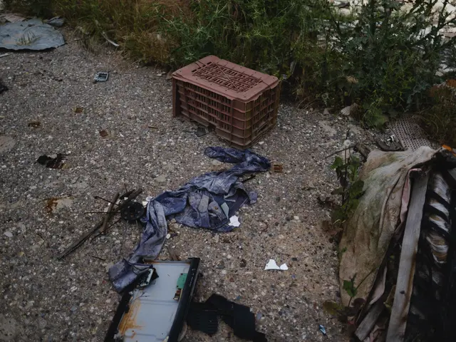 The image shows a pile of trash sitting on the side of a road next to a fence, with a plastic box,...