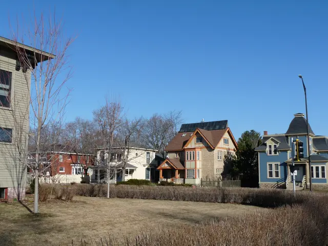 The image shows a row of houses in a residential neighborhood with windows, light poles, trees,...