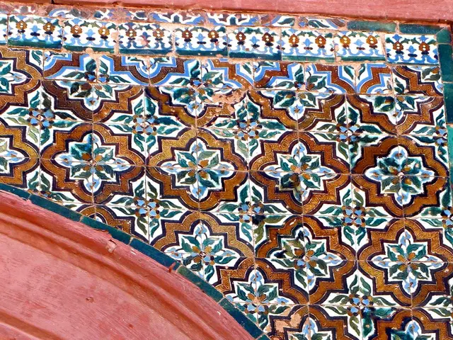 The image shows a close up of a pink building with a colorful tiled wall featuring a unique...