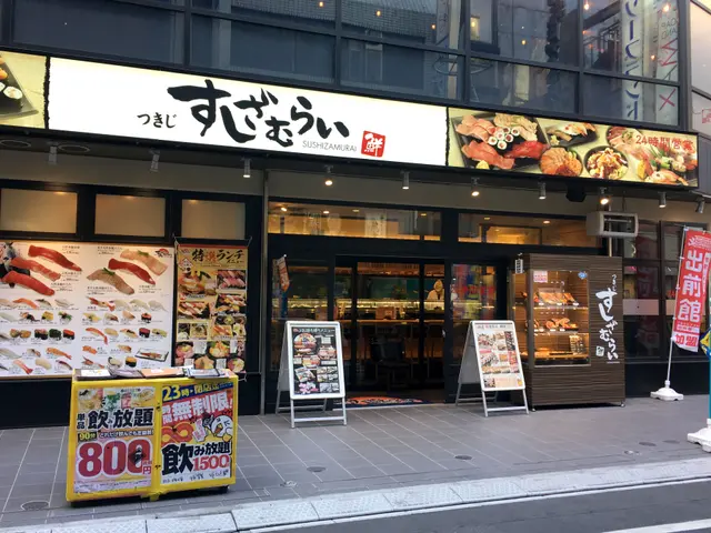 The image shows a sushi restaurant on the corner of a street in Tokyo, Japan. The building has...