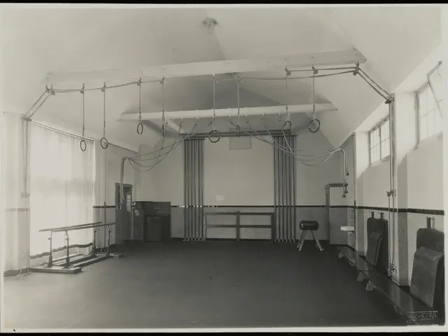 The image shows a black and white photo of a gym with a variety of equipment, including a stool,...