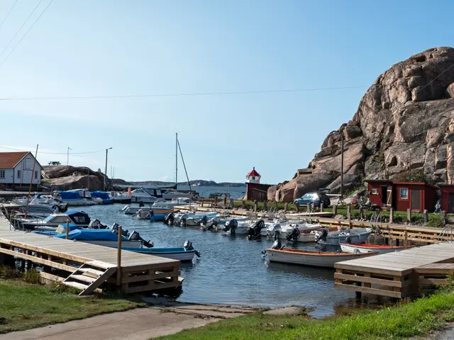 The image shows a marina with boats docked in the water near a rocky shore. On the left side of the...