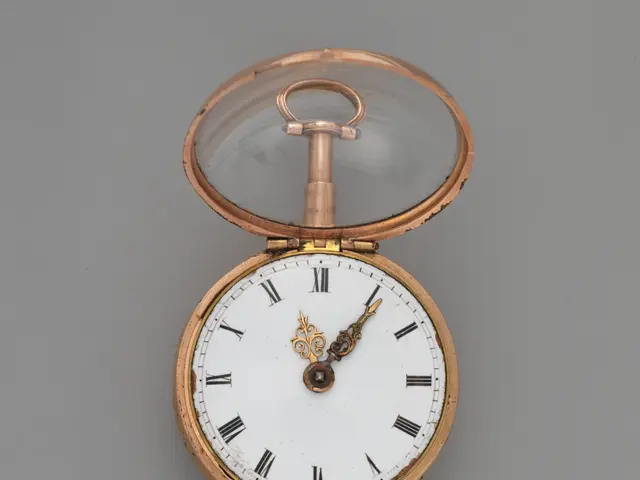 The image shows a gold pocket watch with a white dial featuring Roman numerals on a grey surface....