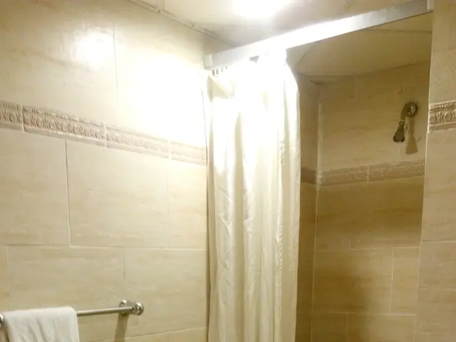 The image shows a bathroom with a shower, a sink, a toilet, a towel on a hanger attached to the...