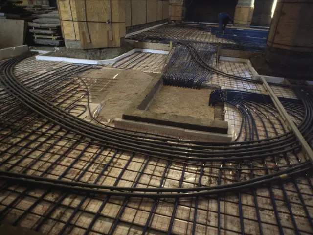 The image shows a construction site with a man working on a floor heating system, surrounded by...