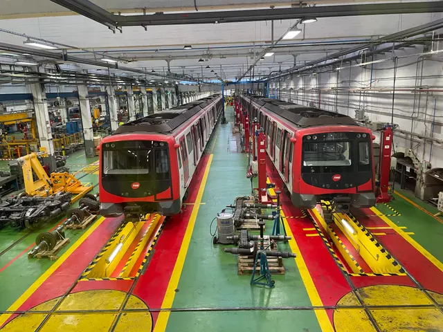 The image shows two trains on the tracks in a large factory, surrounded by machines and other...