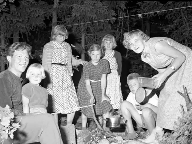 The image shows a black and white photo of a family gathered around a campfire in the woods. There...