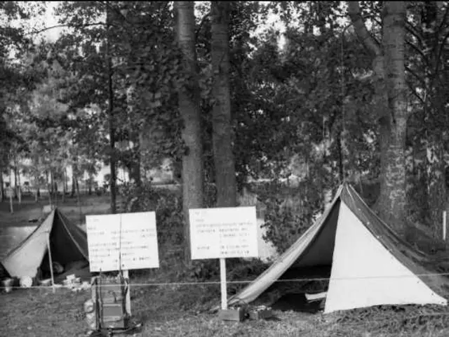 The image shows a black and white photo of a tent set up in the woods, surrounded by trees and...
