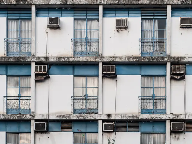 The image shows an old building with many windows and balconies, each with air conditioners...