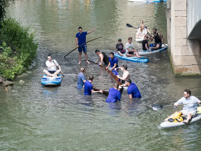 The image shows a group of people in kayaks paddling down a river, with a bridge on the right side...