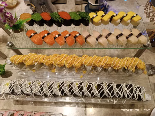 The image shows a display case filled with a variety of sushi on top of a counter, surrounded by...
