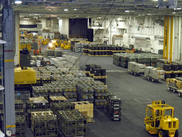 The image shows a large warehouse filled with lots of trucks and containers, as well as people,...