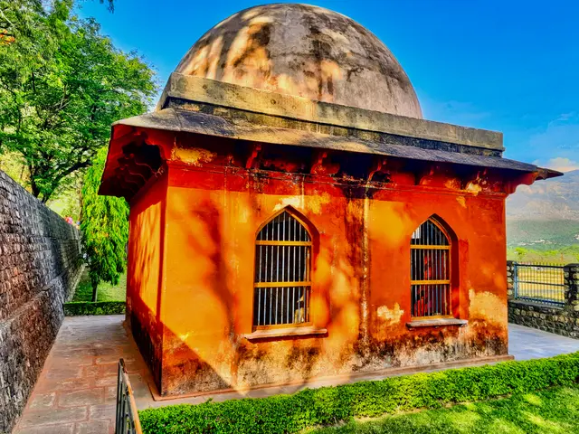 The image shows a small building with a dome on top of it, surrounded by a wall and a railing, with...