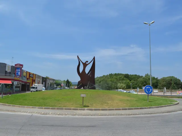 The image shows a large metal sculpture in the middle of a roundabout surrounded by grass, sign...