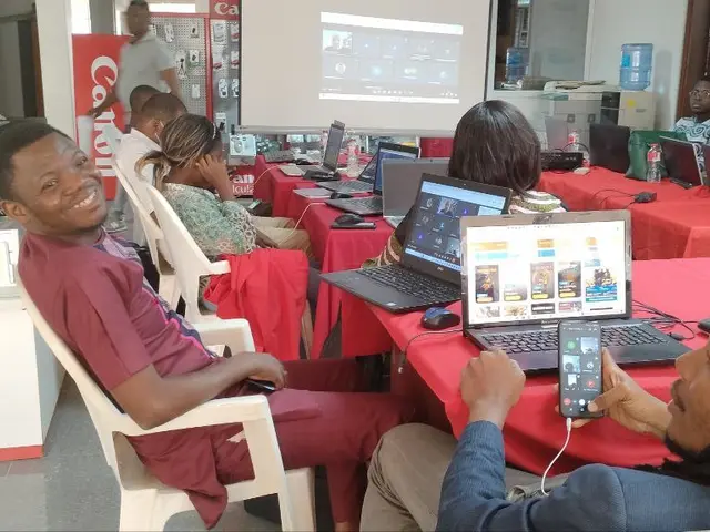 The image shows a group of people sitting around a table with laptops, mouses, bottles, and other...