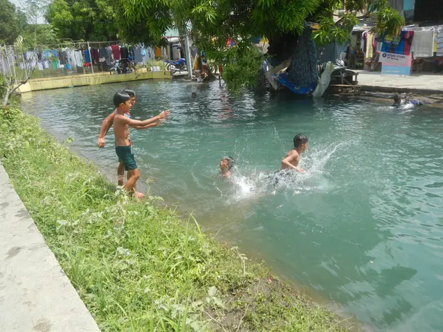The image shows a group of children playing in a pool of water surrounded by lush green grass and...