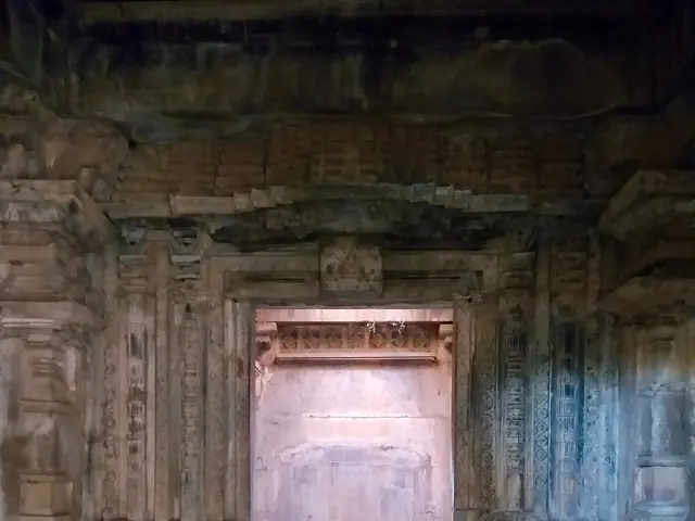 The image shows an old building with carvings on the walls and a doorway in the middle. The walls...