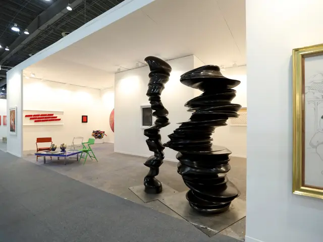 The image shows a room filled with lots of art on display, including sculptures, chairs, tables,...