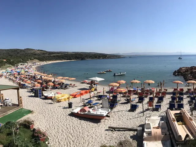 The image shows a beach filled with lots of umbrellas and boats, as well as people enjoying the sun...