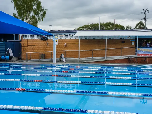 The image shows a large swimming pool with lane dividers in the middle of it, surrounded by a...
