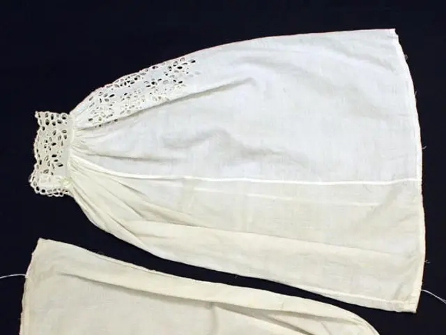 The image shows a pair of white cotton gauze with intricate lace detailing on them, lying on a...