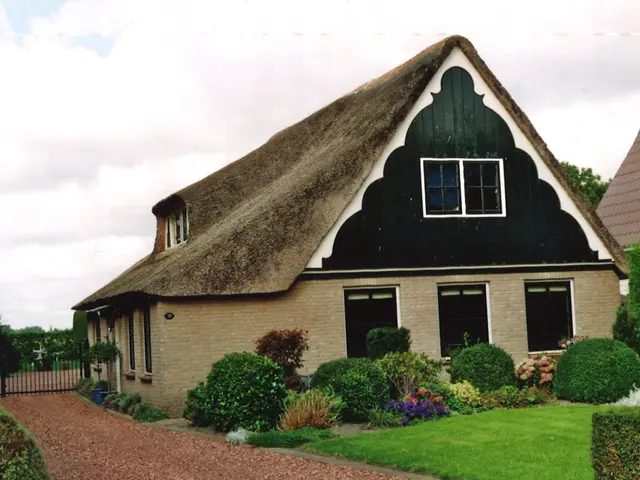 The image shows a house with a thatched roof in the middle of a garden surrounded by plants,...