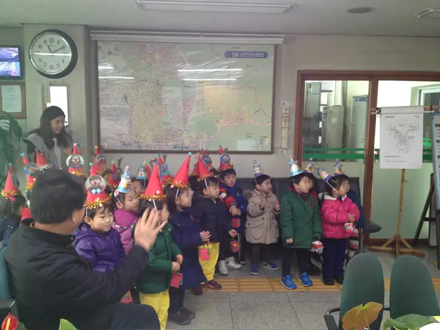 The image shows a group of children standing in front of a map, wearing caps and surrounded by...