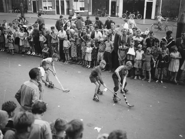 The image shows a group of children playing hockey in front of a crowd of people, some of whom are...