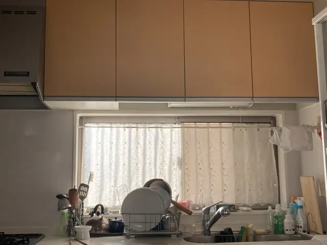The image shows a kitchen with a stove top oven, sink, tap, utensils, spoons in a stand, cupboards,...