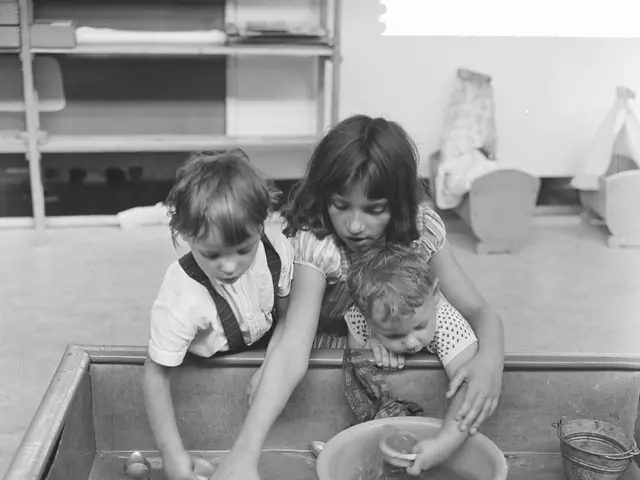 The image shows a black and white photo of three children playing in a sandbox. There is a tub...