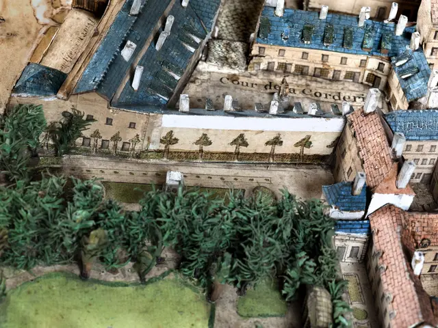 The image shows a model of a city with a lot of buildings, trees, and grass. The model is detailed,...