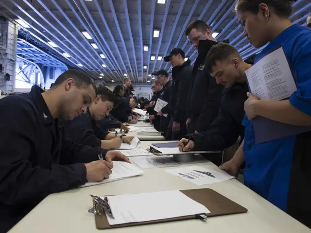 The image shows a group of people sitting at a table in a room, with papers and files spread out in...