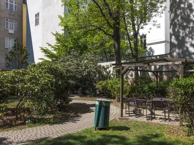 The image shows a park with a green trash can sitting in the middle of it, surrounded by grass,...