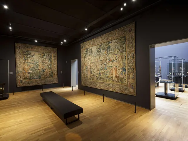 The image shows a room filled with lots of paintings on the walls, a bench on the floor, poles with...