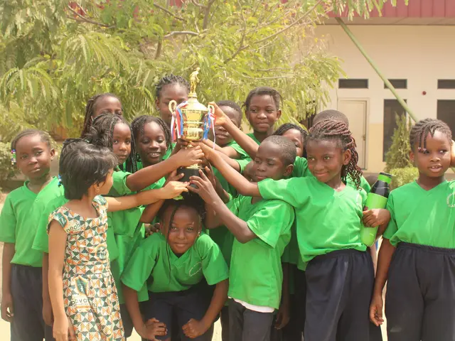 The image shows a group of children standing next to each other, proudly holding up a trophy. In...