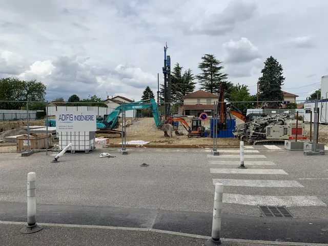 The image shows a construction site with a lot of construction equipment on the side of it,...